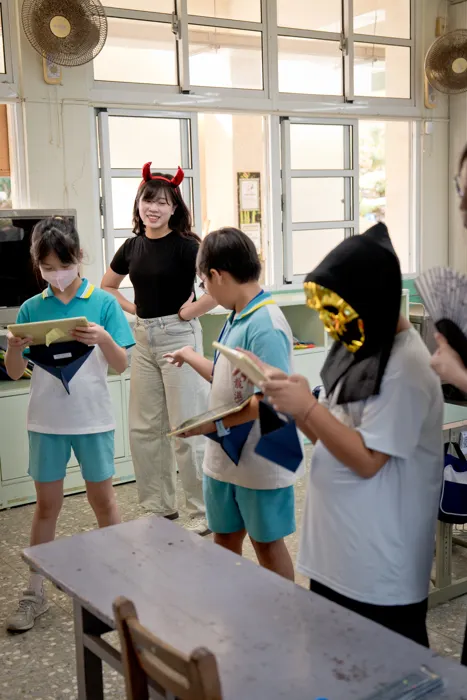 學生拿著學習材料，在老師陪伴下參與教室活動